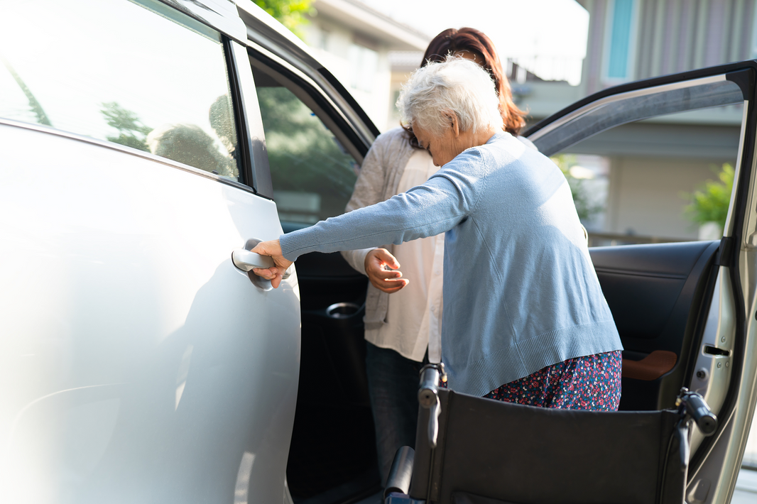 Transporte especializado y movilidad segura para adultos mayores en El Salvador: Una integrante del Juby Care Team asiste a una mujer de la tercera edad que utiliza silla de ruedas a subir a un vehículo de forma segura, garantizando el bienestar, seguridad y acompañamiento integral de los grandes de la casa.