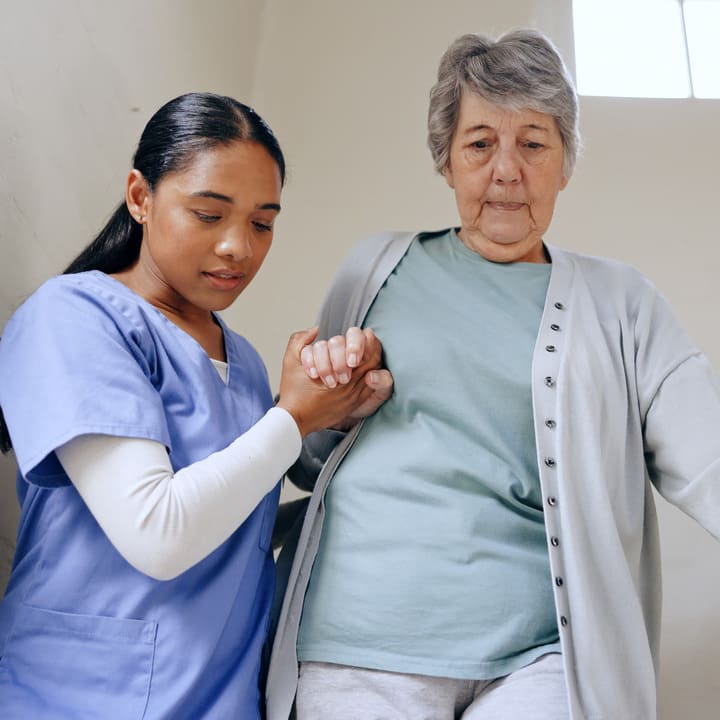 Movilidad segura y acompañamiento para adultos mayores en El Salvador: Una enfermera del Juby Care Team brinda asistencia física y apoyo en el desplazamiento de una paciente de la tercera edad, garantizando un cuidado especializado con calidez humana y respeto en su hogar.