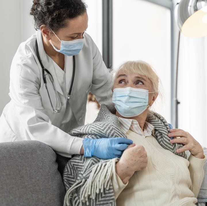 Cuidados de enfermería a domicilio y protocolos de bioseguridad para adultos mayores en El Salvador: Una profesional del Juby Care Team, con mascarilla y guantes, brinda atención personalizada y segura a una paciente de la tercera edad en su hogar, garantizando bienestar y protección integral.